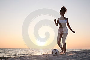 African American woman playing football on beach at sunset. Space for text