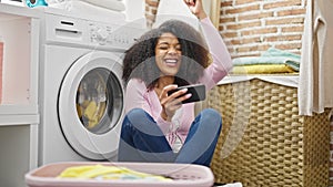 African american woman playing video game waiting for washing machine at laundry room