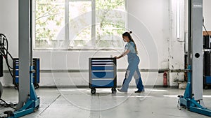 African american woman, professional female mechanic pulling, carrying tool box cart in auto repair shop. Car service