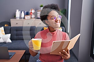 African american woman reading book and drinking coffee sitting on sofa at home