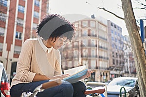 African American woman reading a book sitting on a bench. Latina woman with a book.