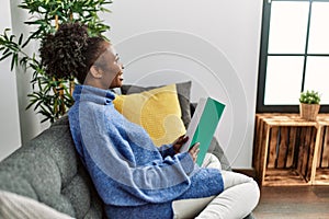 African american woman reading book sitting on sofa at home