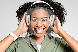 An African-American woman in a relaxed olive green shirt smiles brightly while enjoying music