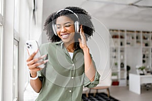 An African-American woman in a relaxed olive green shirt smiles brightly while enjoying music