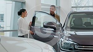 African American woman saleswoman seller consultant auto dealer help man customer buyer examine automobile choose new