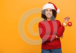 African American woman in santa claus hat on orange background, Happy woman holds in hands christmas balls. Xmas concept