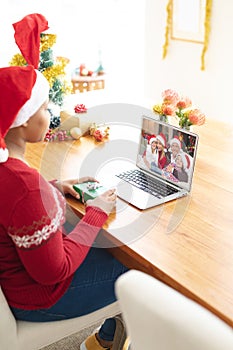 African american woman in santa hat making laptop christmas video call with family in santa hats