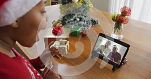 African american woman with santa hat using tablet for christmas video call with family on screen