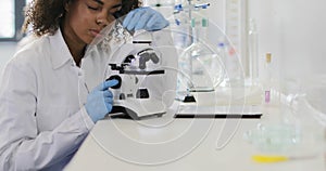 African american woman scientist working with microscope in modern laboratory making analysis