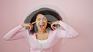 African american woman screaming loudly covering ears with fingers over isolated pink background