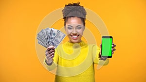 African-American woman showing smartphone and bunch of dollars, money transfer