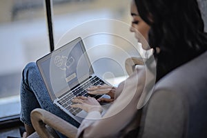 An african american woman sitting an armchair and typing on laptop keyboard