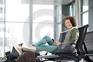 African american woman sitting on bench with luggage and mobile phone