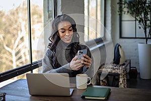 An African-American woman sitting at the table by the window and using cellphone