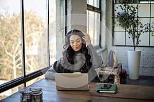 An African-American woman sitting at the table by the window and working on her laptop