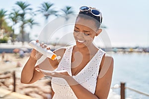 African american woman smiling confident applying sunscreen lotion at seaside