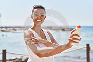 African american woman smiling confident applying sunscreen lotion at seaside