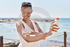 African american woman smiling confident applying sunscreen lotion at seaside