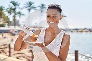 African american woman smiling confident applying sunscreen lotion at seaside