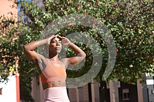 African American woman in sportswear covering her eyes with her hands to protect herself from the sun on an outdoor bench. Concept