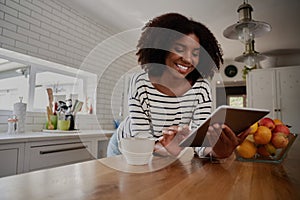 African American Woman standing in kitchen leaning on counter using digital tablet looking at online recipes