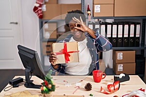 African american woman standing by manikin at small business on christmas smiling happy doing ok sign with hand on eye looking