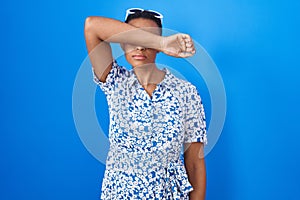 African american woman standing over blue background covering eyes with arm, looking serious and sad