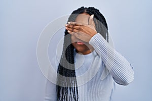 African american woman standing over blue background covering eyes with hand, looking serious and sad