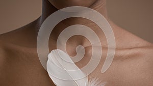 African American Woman Stroking Skin With Feather, Beige Background, Cropped