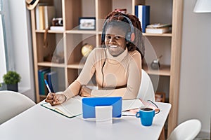 African american woman student listening to music writing on notebook at home