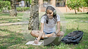 African american woman student using laptop and headphones taking notes at university campus