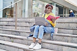 African american woman student using laptop reading book at university