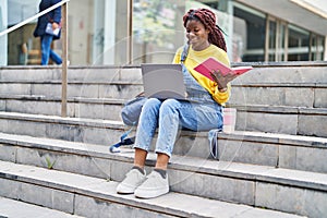 African american woman student using laptop reading book at university