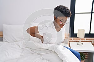 African american woman suffering for knee injury sitting on bed at bedroom