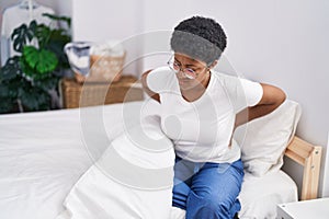 African american woman suffering for knee injury sitting on bed at bedroom