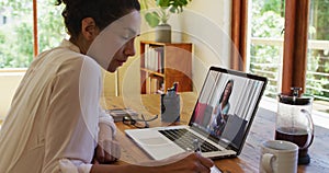 African american woman taking notes while having video call with female colleague on laptop at home