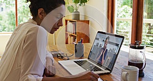 African american woman taking notes while having a video call on laptop at home