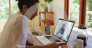 African american woman taking notes while having video call with male colleague on laptop at home