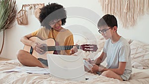African American Woman teaches boy to play guitar using laptop.