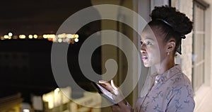 African American woman uses a tablet at night on a balcony, with copy space