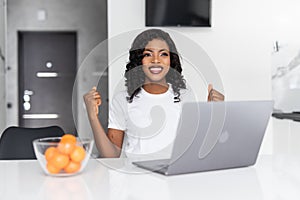 African american woman using laptop at kitchen very happy and excited, winner expression celebrating victory screaming with big