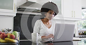 African american woman using laptop in the kitchen while working from home