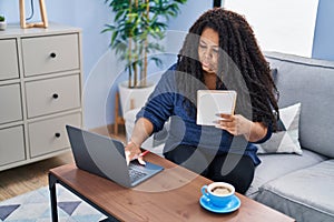 African american woman using laptop reading notebook at home