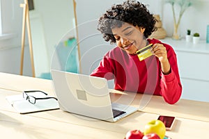 African american woman using laptop shopping online paying with gold credit card. Girl sitting at home buying on