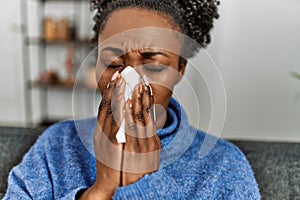 African american woman using napkin sitting on sofa at home