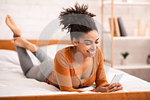 African American Woman Using Smartphone Lying In Bed At Home