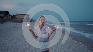 African american woman walking, dancing, having fun on night party at seaside with sparklers lights in hands on Fourth