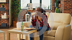 African american woman watching tv and eating pizza