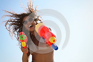 African American woman with water guns against blue sky, low angle view. Space for text