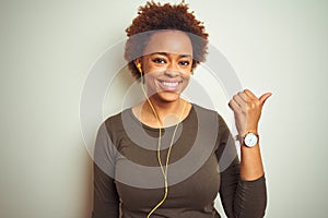 African american woman wearing earphones listening to music over isolated background smiling with happy face looking and pointing